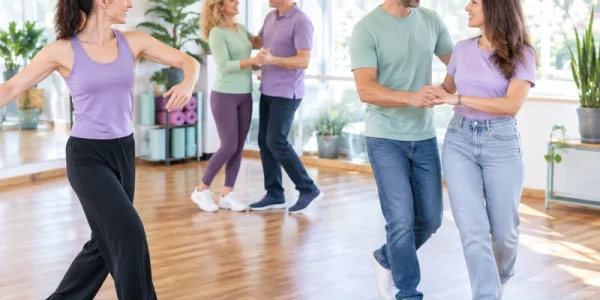 מדריכה ושני זוגות מבוגרים מתרגלים צעדי ריקוד באולם מואר כחלק מפעילות זוגית משותפת